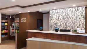A hotel reception area with a 'Corner Market' sign, a reception desk, a refrigerator, and a wall with a tree branch pattern. - Fairfield Inn and Suites by Marriott Austin South (Austin)