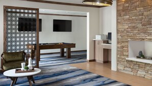 A modern room with a pool table, a sofa, a small round table with a tray, a stone accent wall, and a television mounted on the wall. - Fairfield Inn and Suites by Marriott Austin South (Austin)