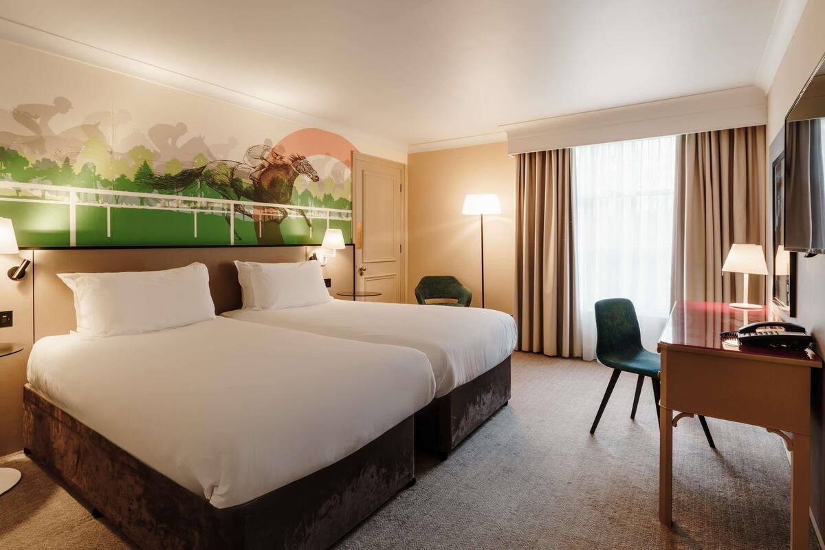 Una habitación de hotel con una cama grande, un escritorio, una silla, una lámpara y un mural en la pared.