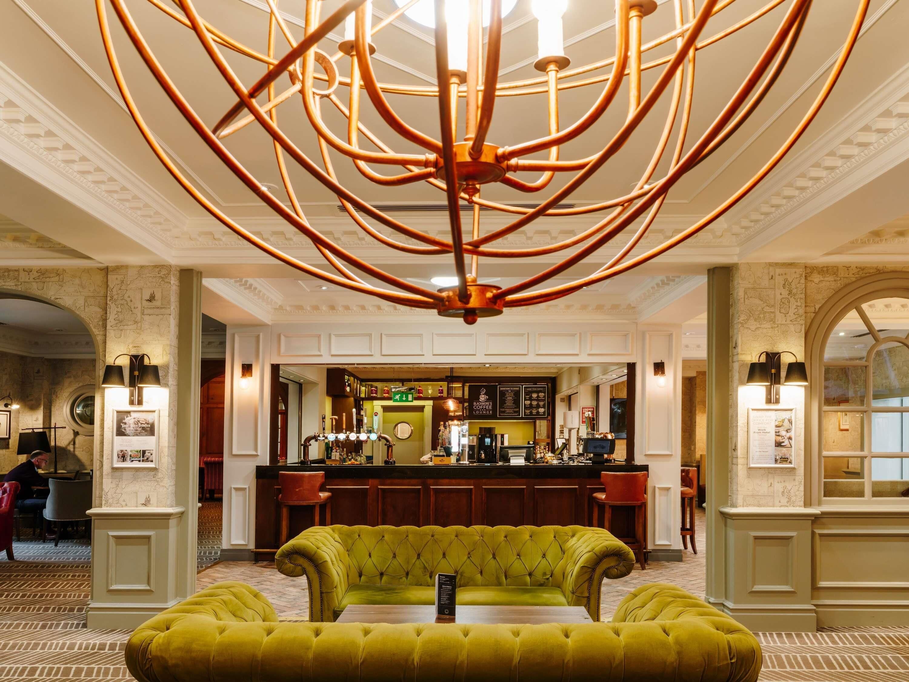 Una hall con un divano verde trapuntato, un'area bar e un lampadario.