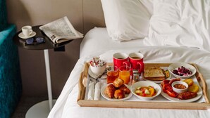 A neatly made breakfast tray on a bed with white linens, a newspaper, and a cup on a side table.
