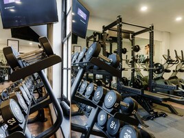 Un gimnasio con equipo de levantamiento de pesas, cintas de correr y un televisor mostrando BBC Radio.