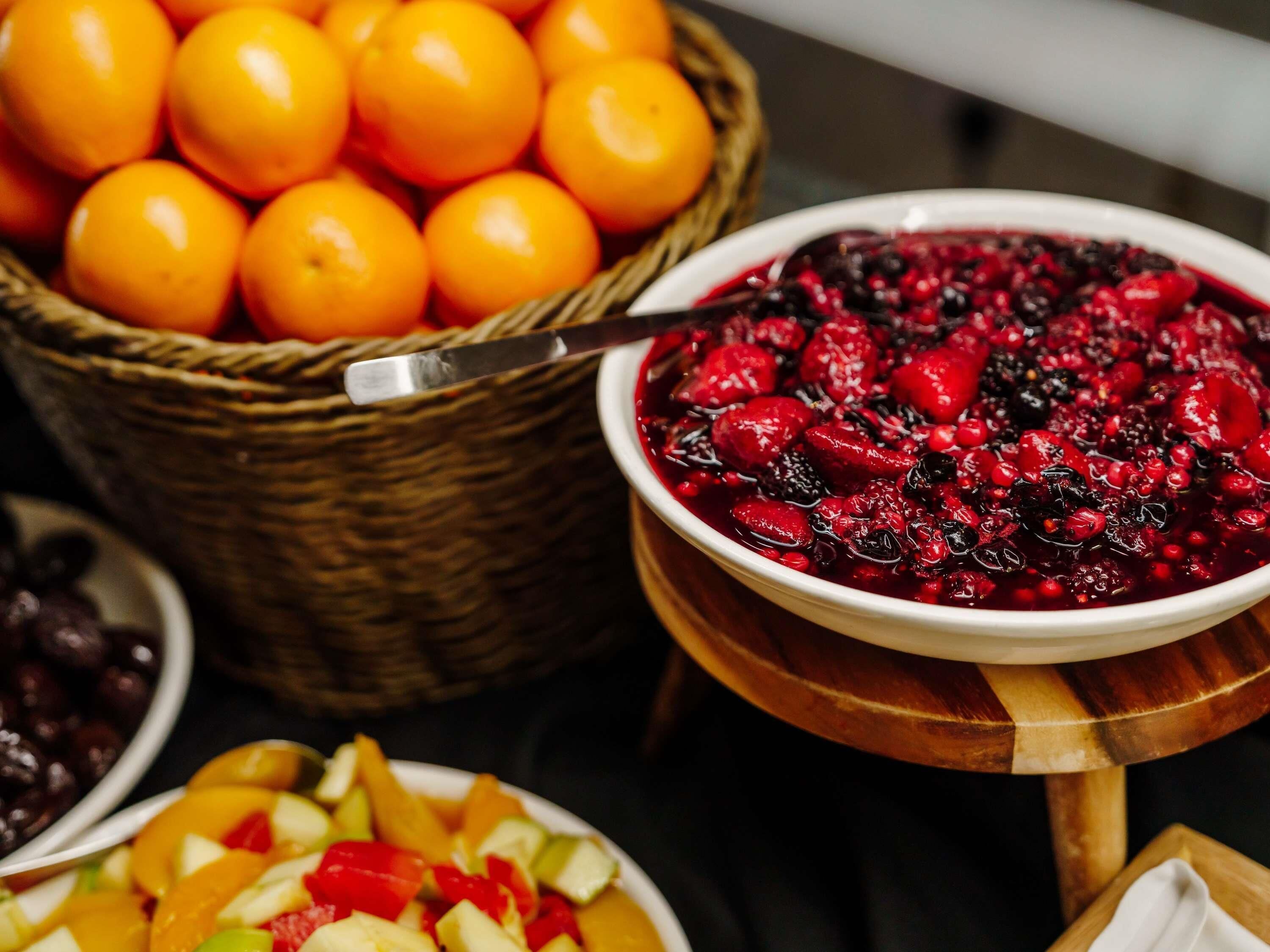 A table with a bowl of mixed berries, a basket of oranges, and a bowl of sliced fruit.