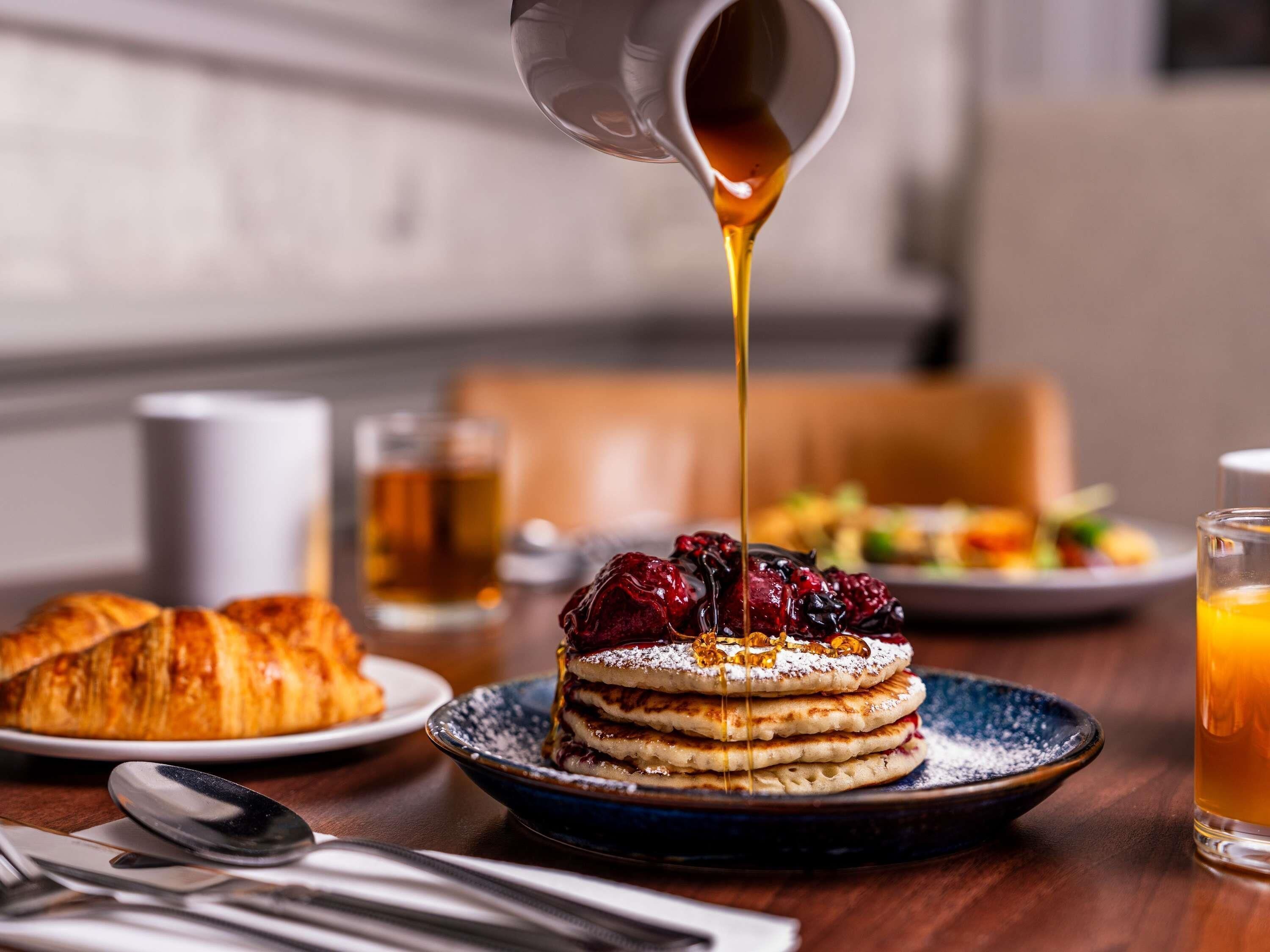 A breakfast setting with pancakes, a croissant, and a glass of orange juice.