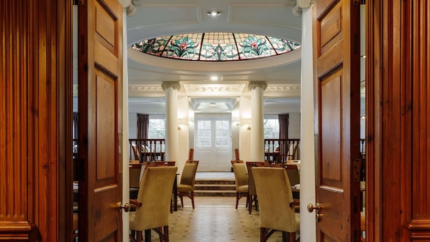 A grand entrance with a stained glass ceiling, a central staircase, and a dining area with wooden chairs and tables.