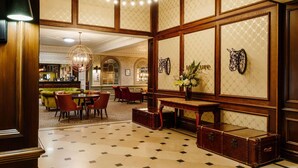 A hotel lobby with a checkered floor, a chandelier, a reception desk, and a bar area.