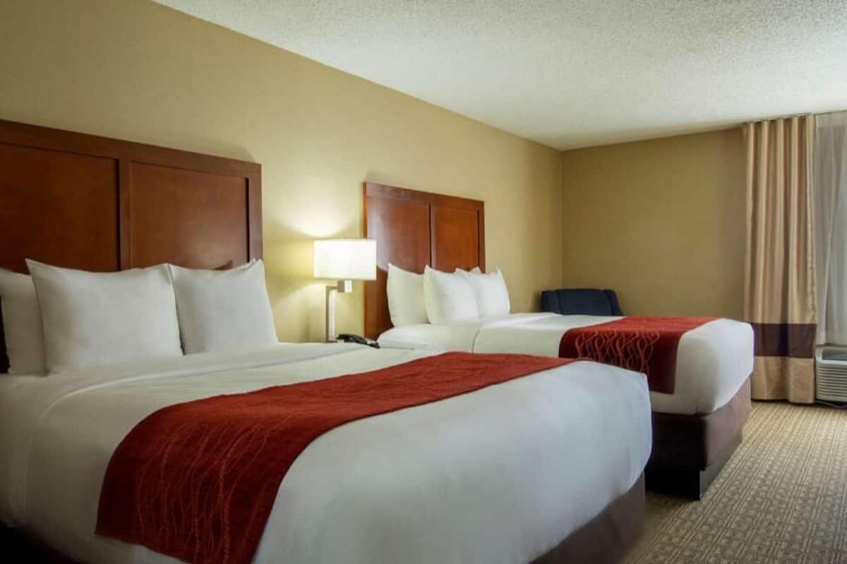 A hotel room with two beds, a desk, a lamp, and a window with curtains.