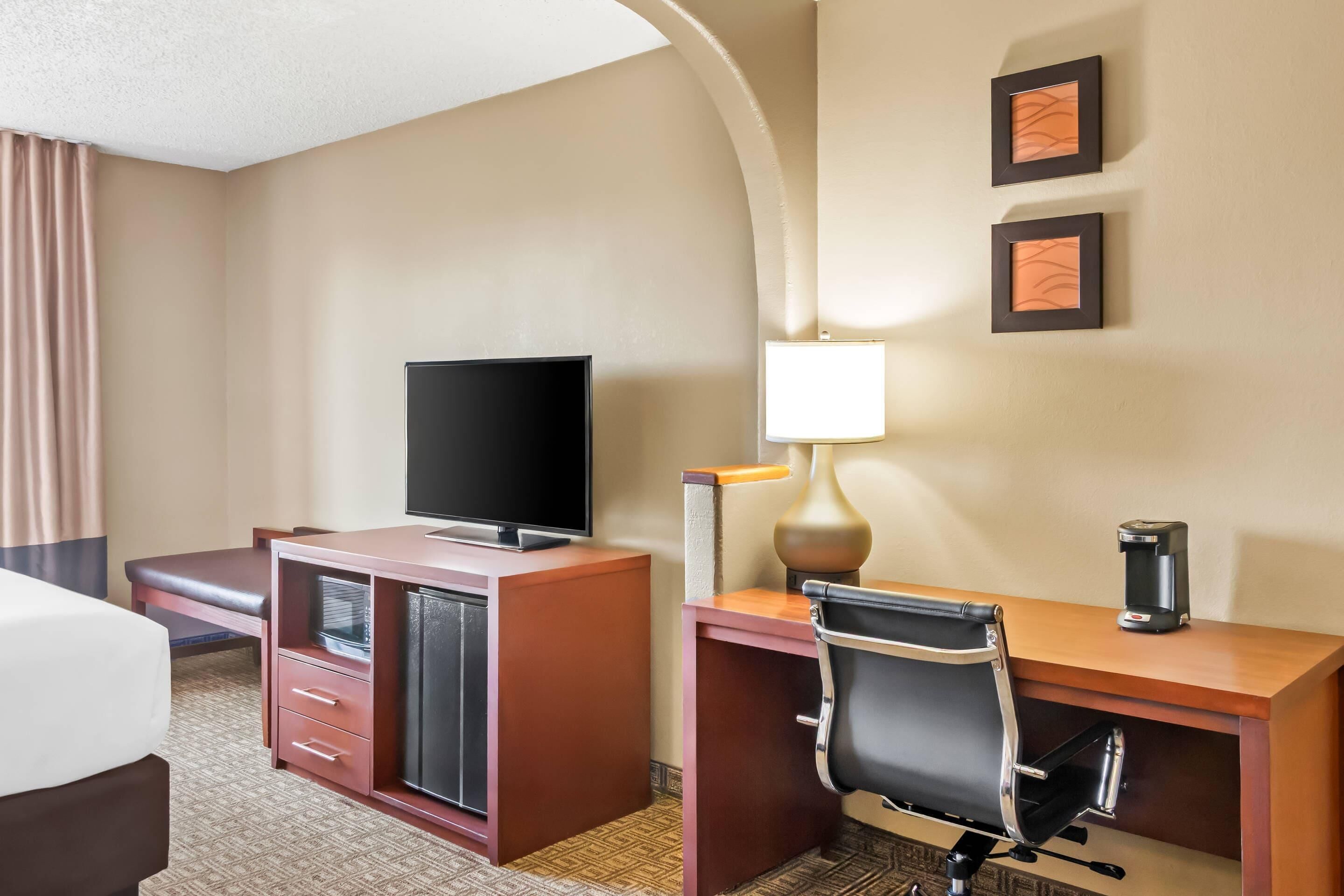 A hotel room with a bed, a desk with a chair, a television, a lamp, and a coffee maker.