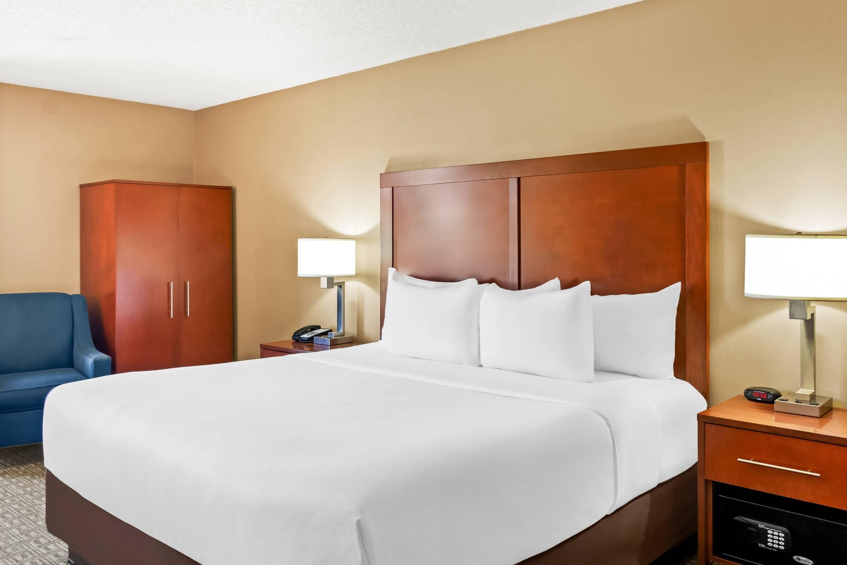 A hotel room with a large bed, a wardrobe, a desk with a lamp, and a blue chair.