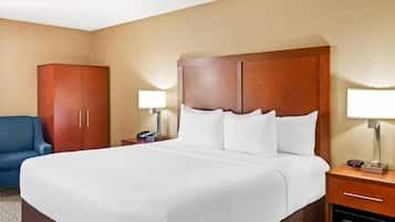 A hotel room with a large bed, a wardrobe, a desk with a lamp, and a blue chair.