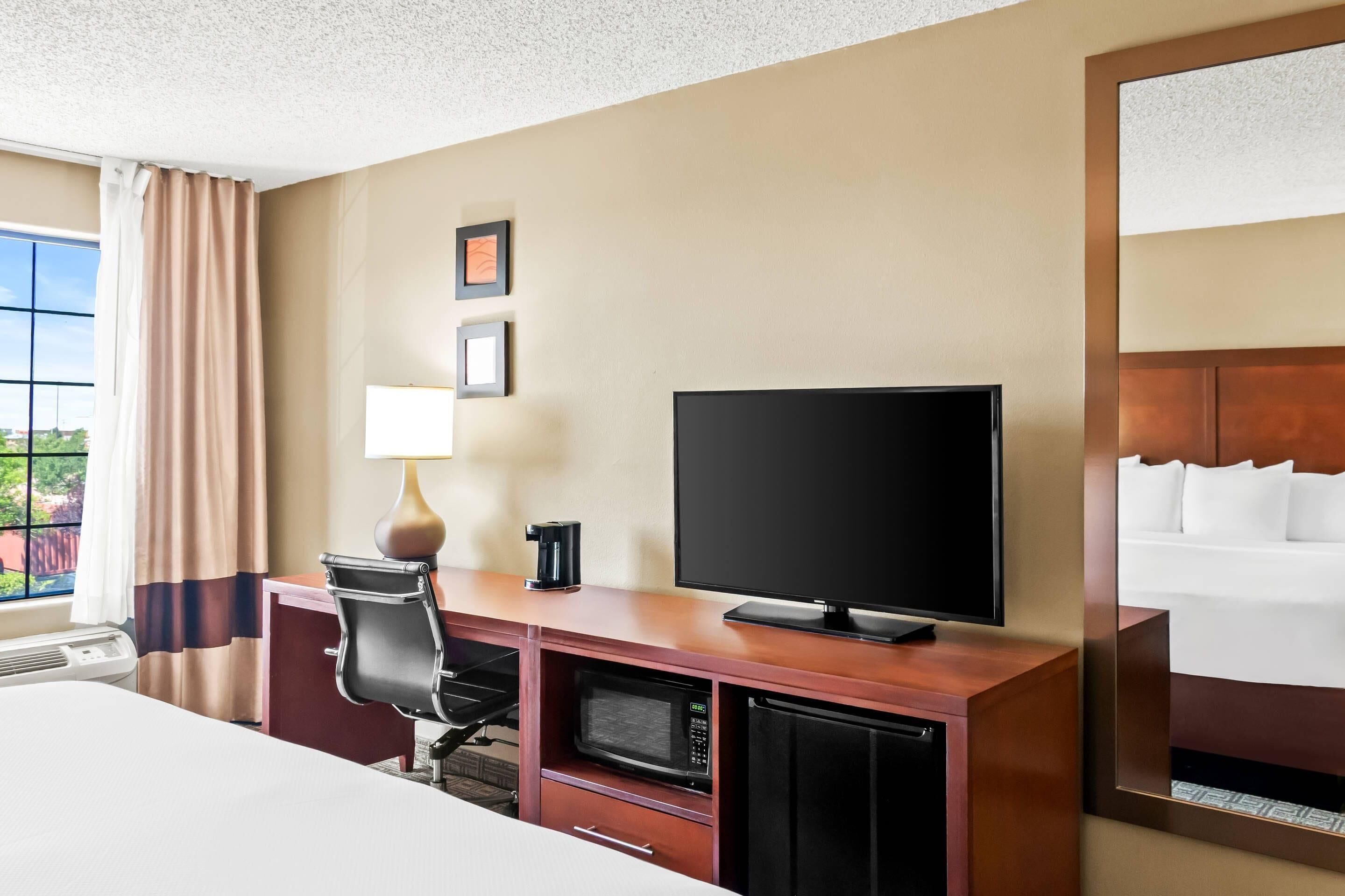 A hotel room with a bed, a desk with a television, a microwave, and a coffee maker.