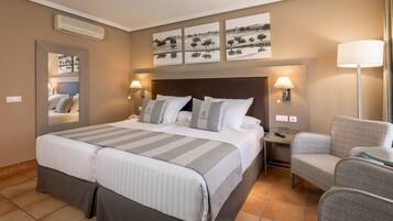 Quarto de hotel com uma cama grande, duas mesas de cabeceira, uma cadeira e uma televisão na parede.