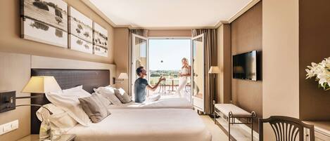 A hotel room with two beds, a TV, a desk, and a balcony with a view.