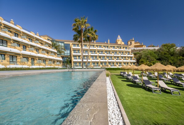 Relax by the large pool surrounded by lush greenery and lounge chairs, with stunning views from the hotel's modern balconies.