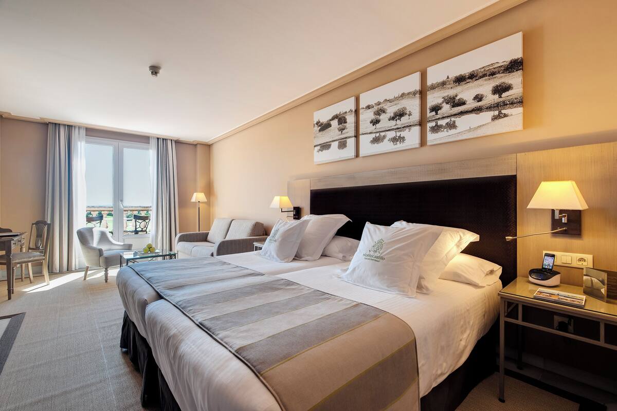 A hotel room with a large bed, two bedside tables, a desk, and a chair. There are three wall-mounted artworks above the bed.