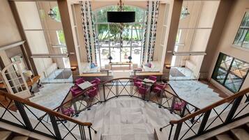A spacious lobby with a marble floor, a central seating area with purple chairs, and large windows offering a view of the outdoors.