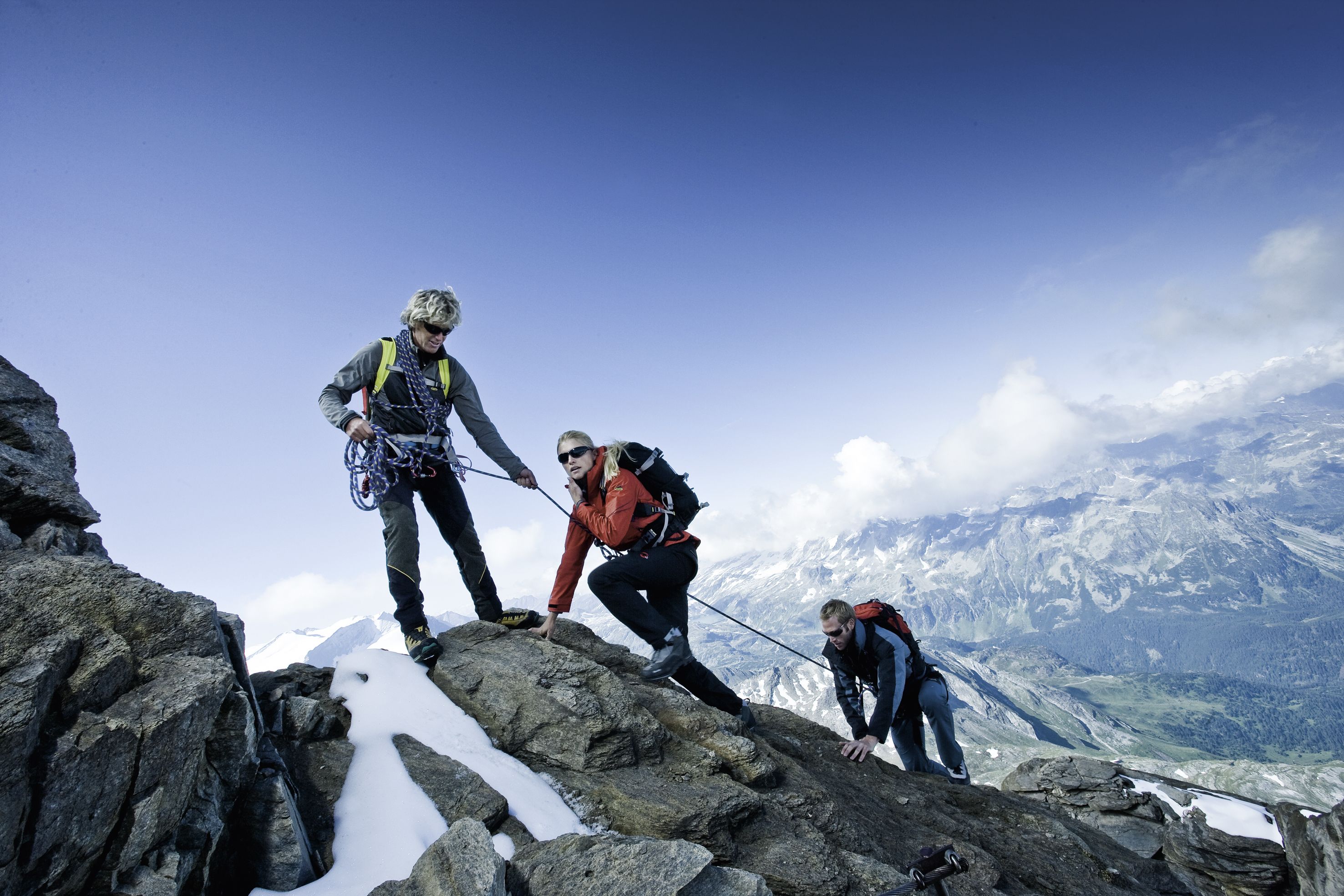 Three hikers on a snowy mountain peak with a clear sky and snow-covered landscape in the background.