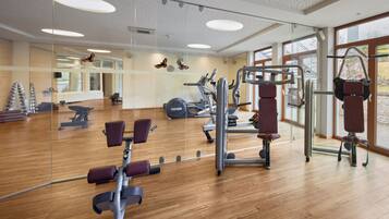 Un gimnasio con equipo de ejercicio, amplias ventanas y suelo de madera.