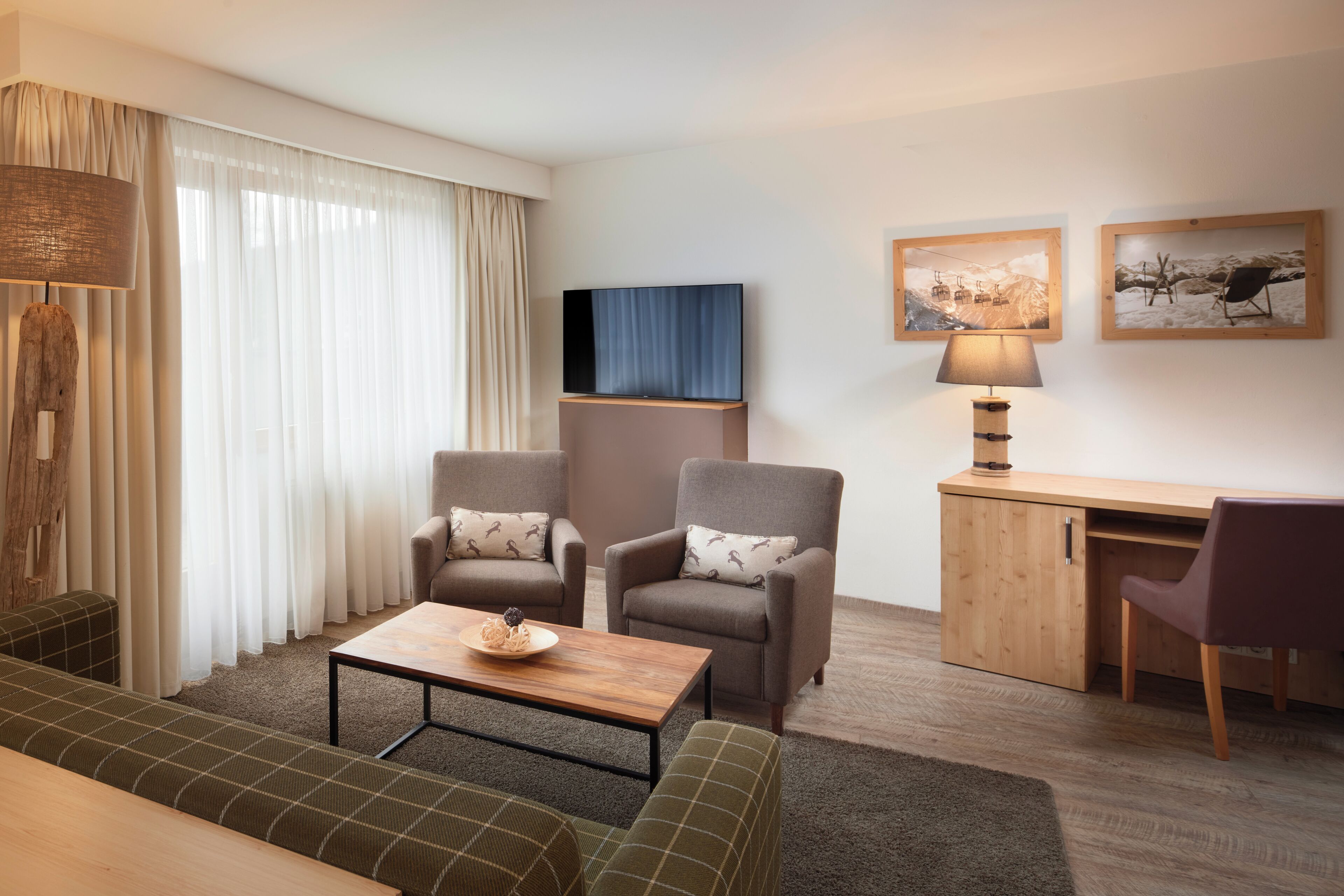 Een moderne woonkamer met een bank, twee fauteuils, een salontafel, een bureau en een televisie.