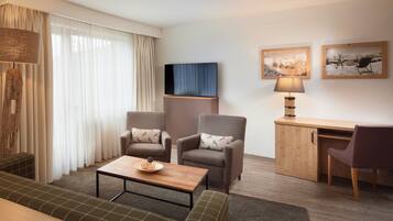 Een moderne woonkamer met een bank, twee fauteuils, een salontafel, een bureau en een televisie.