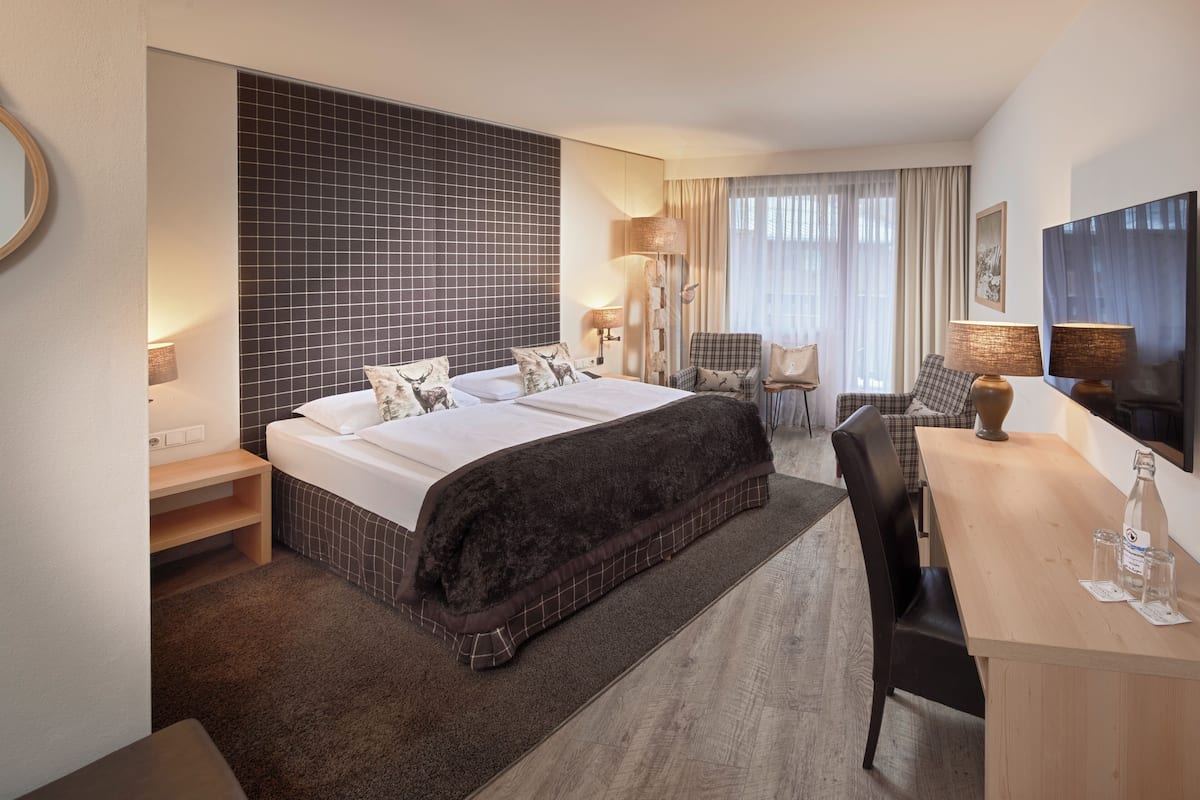 Una habitación de hotel con una cama grande, un escritorio, una silla, una lámpara y una ventana con cortinas.