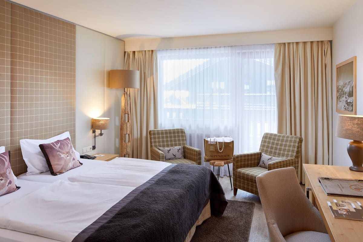 Habitación de hotel con una cama grande, dos sillones, una mesita y un escritorio con lámpara.