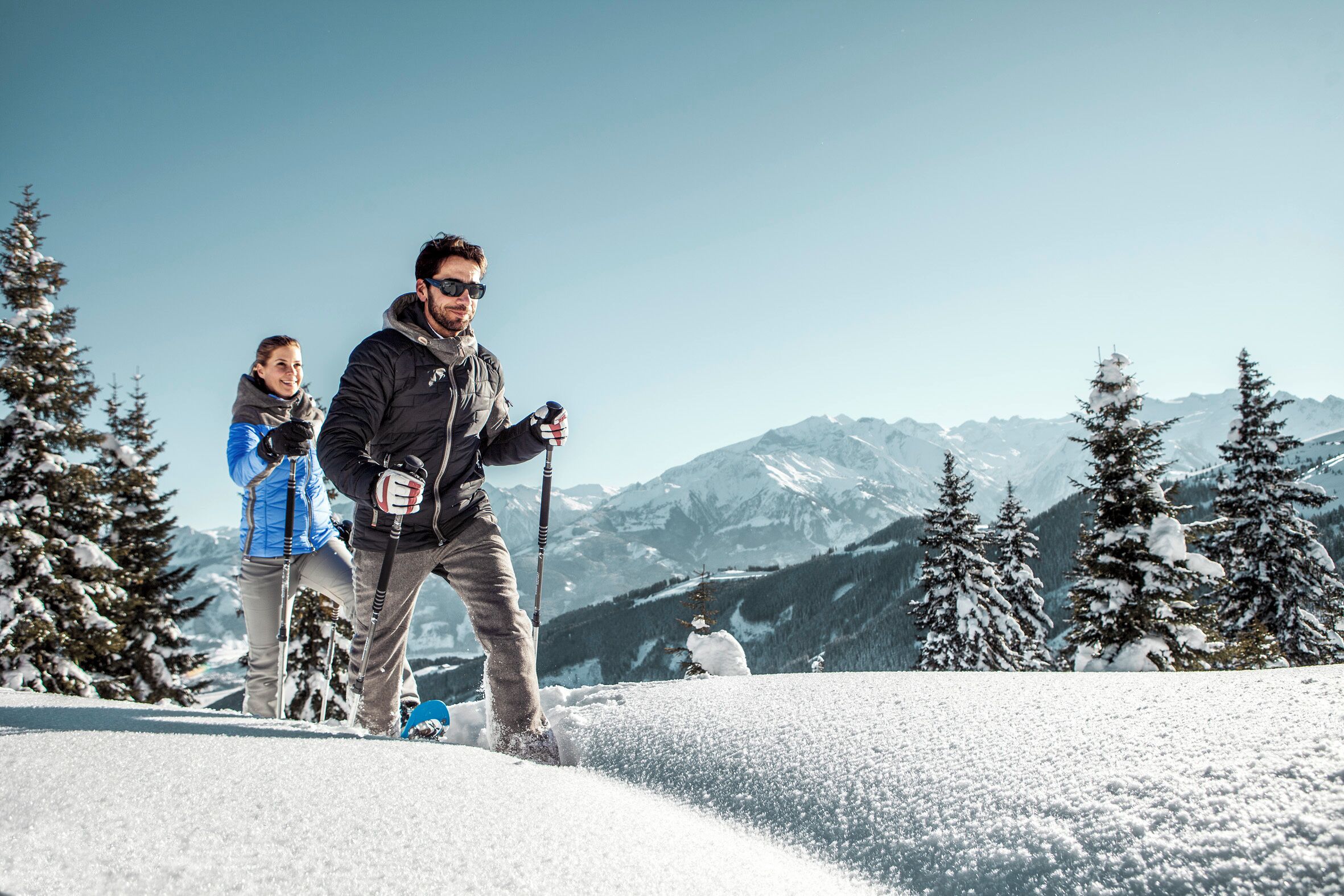 A person skiing on a snowy slope with a clear view of snow-covered mountains and trees in the background.