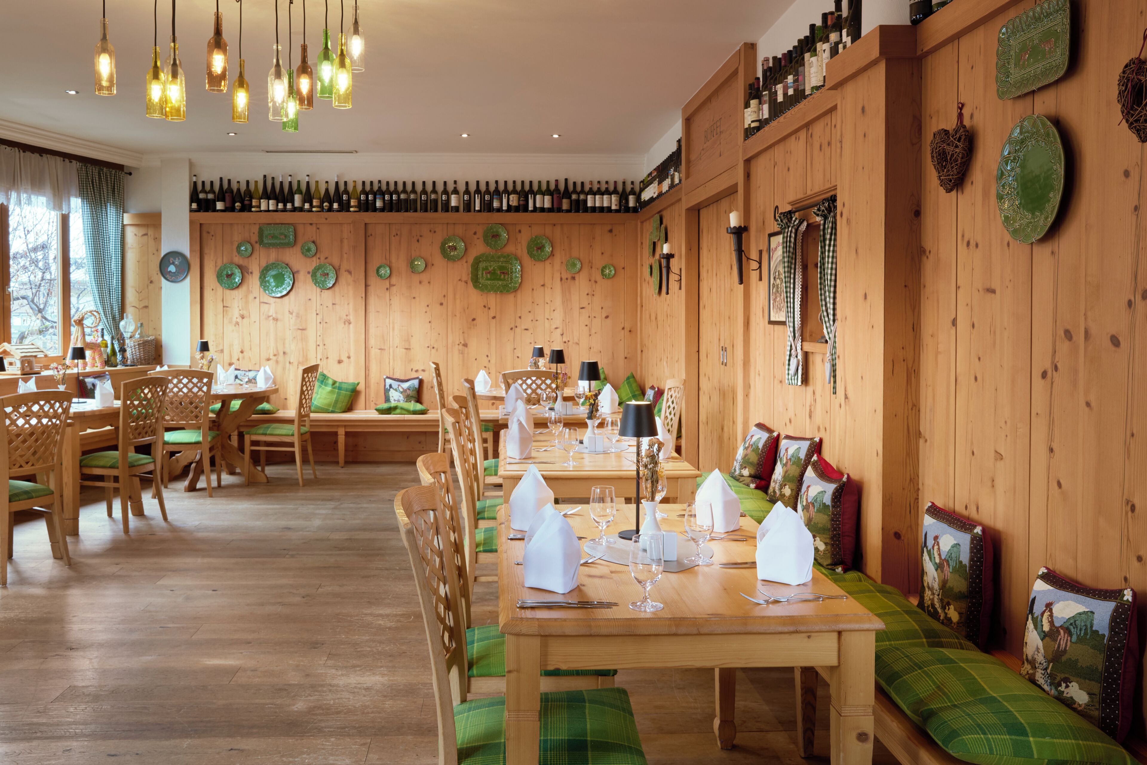 A restaurant with wooden walls, green upholstered seating, and a wine rack.