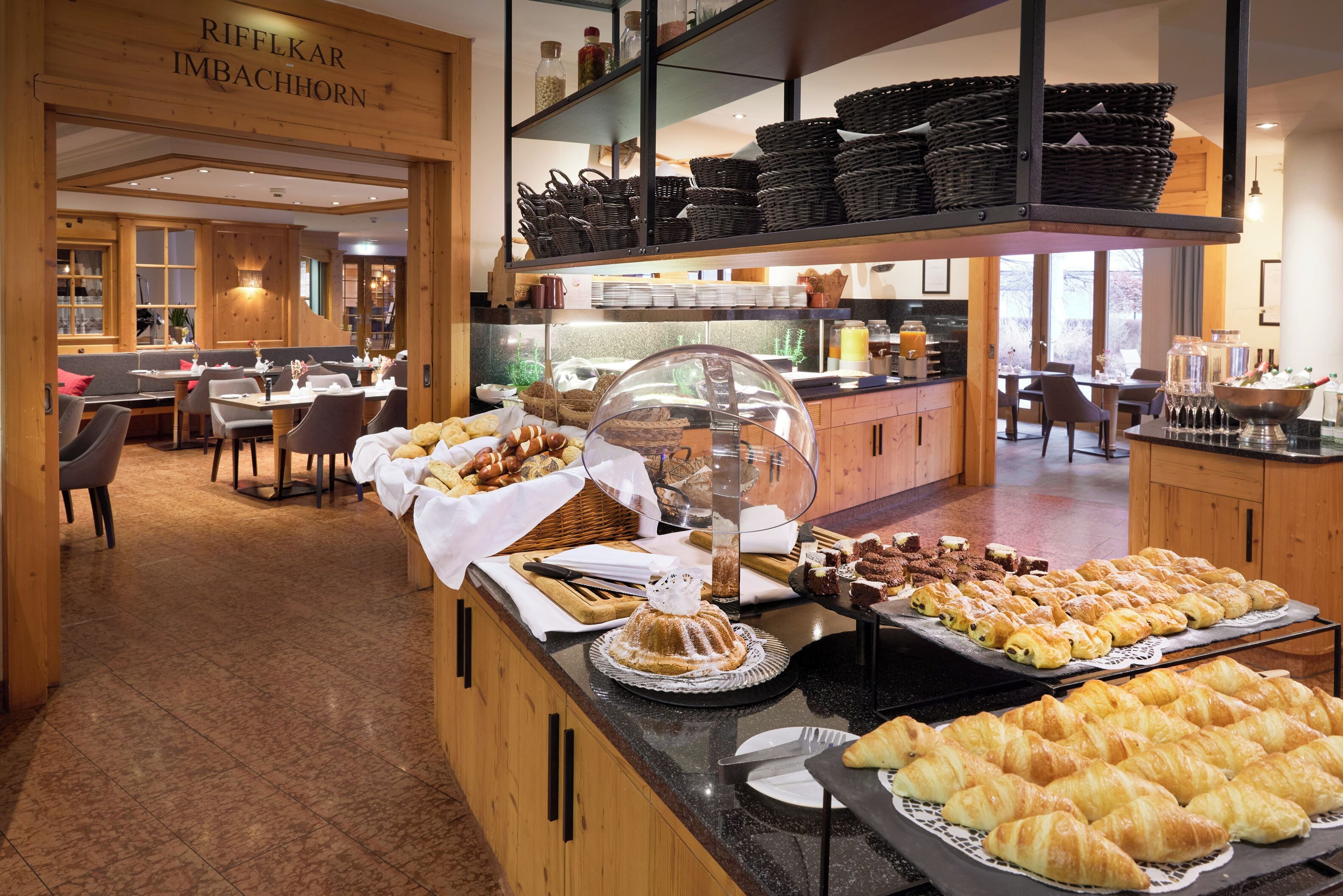 A buffet area with various baked goods, a seating area with tables and chairs, and a wooden interior design.