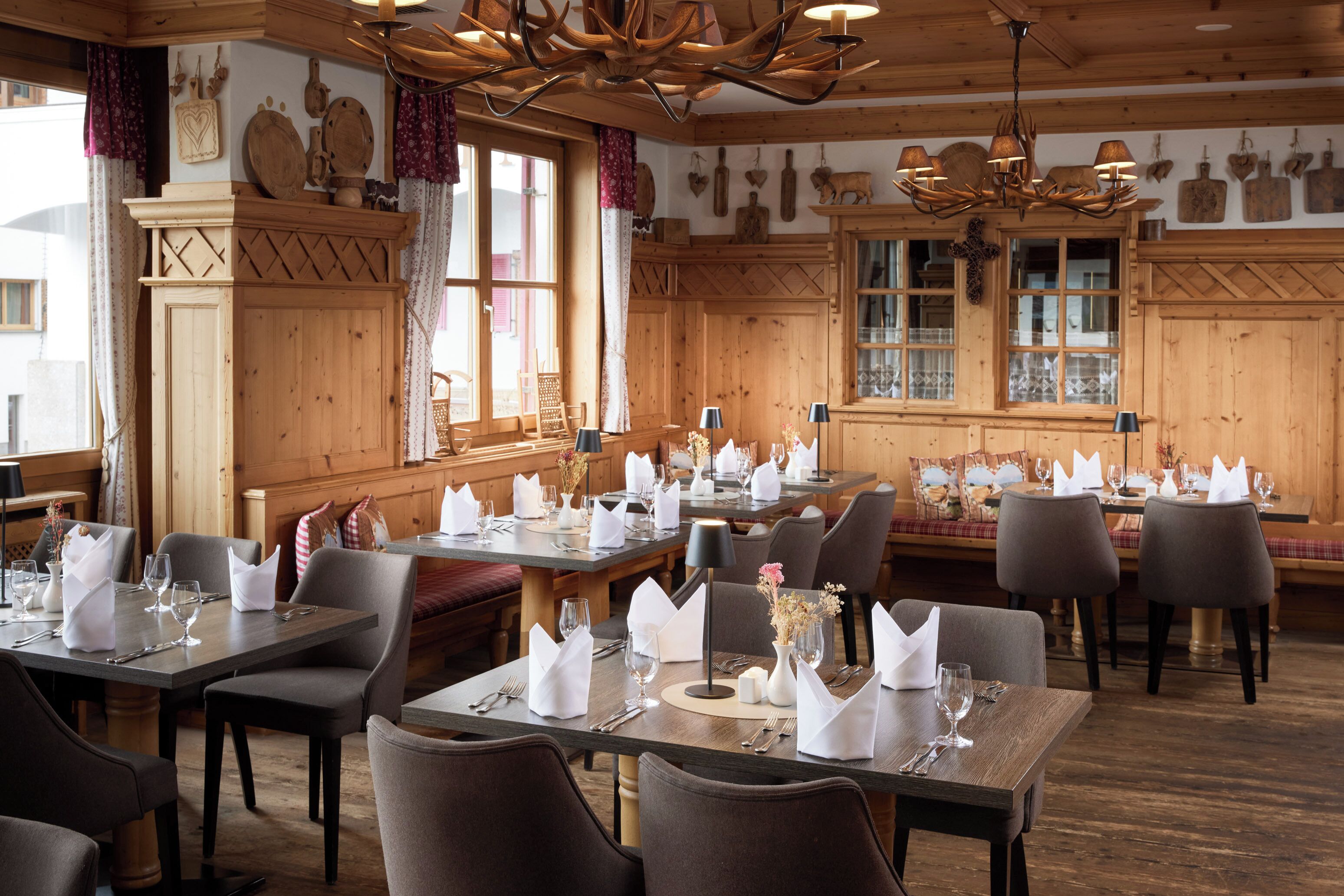 A restaurant with wooden interiors, multiple dining tables set with white napkins, and a chandelier.