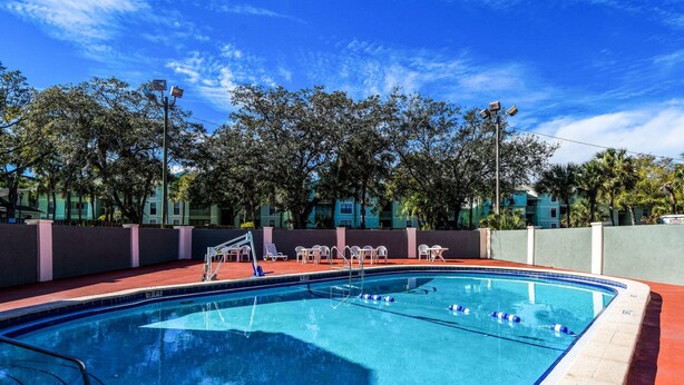 Una piscina con indicador de profundidad de 3 pies, rodeada por un suelo rojo y sillas blancas.