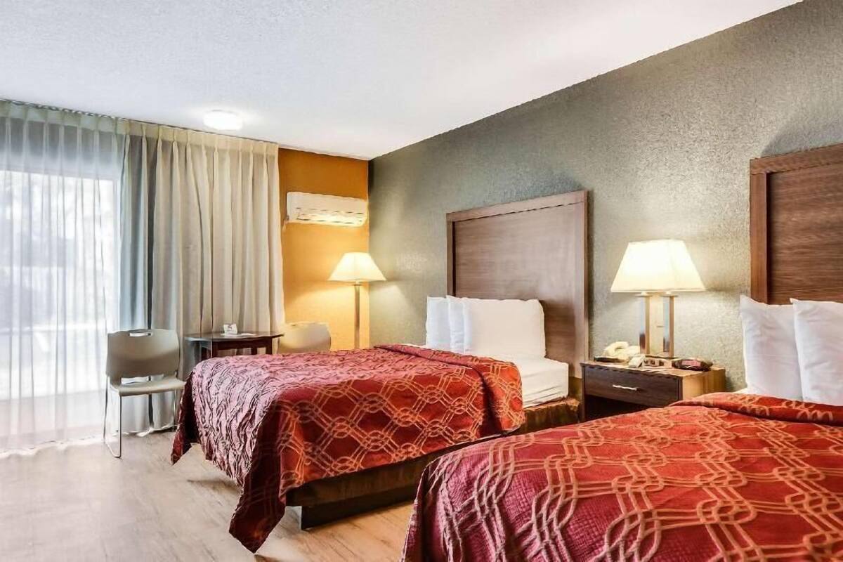 Ein Hotelzimmer mit zwei Betten, einem Schreibtisch, einem Stuhl und einem Fenster mit Vorhängen.