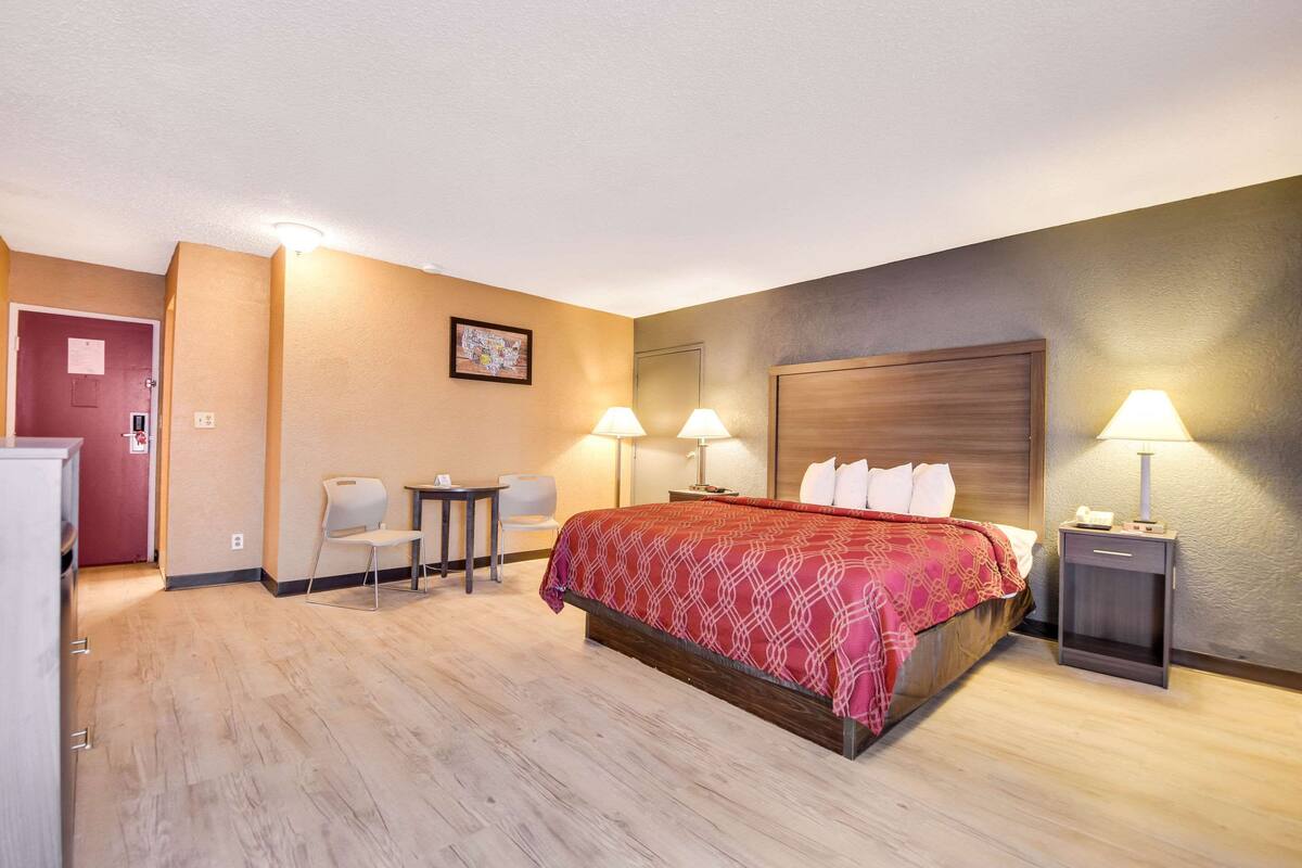 Ein Hotelzimmer mit einem Bett, zwei Nachttischen mit Lampen, einem Schreibtisch mit Stuhl sowie einem kleinen Tisch mit Stuhl.