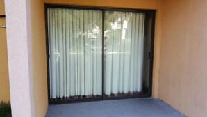 Una puerta corredera de vidrio con una cortina blanca, ubicada en un edificio con fachada amarilla.