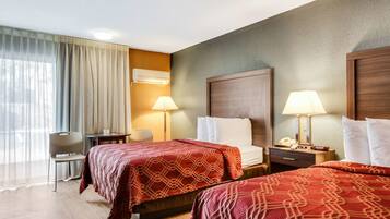 A hotel room with two beds, a desk, a chair, and a lamp.