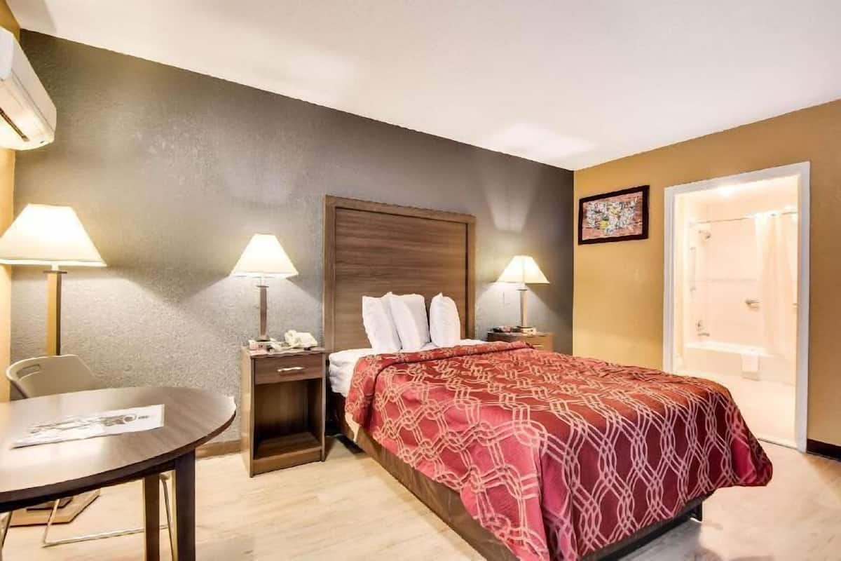 Ein Hotelzimmer mit einem Bett, zwei Nachttischlampen, einem Schreibtisch mit Stuhl, einem kleinen Tisch und einer Tür zu einem Badezimmer.