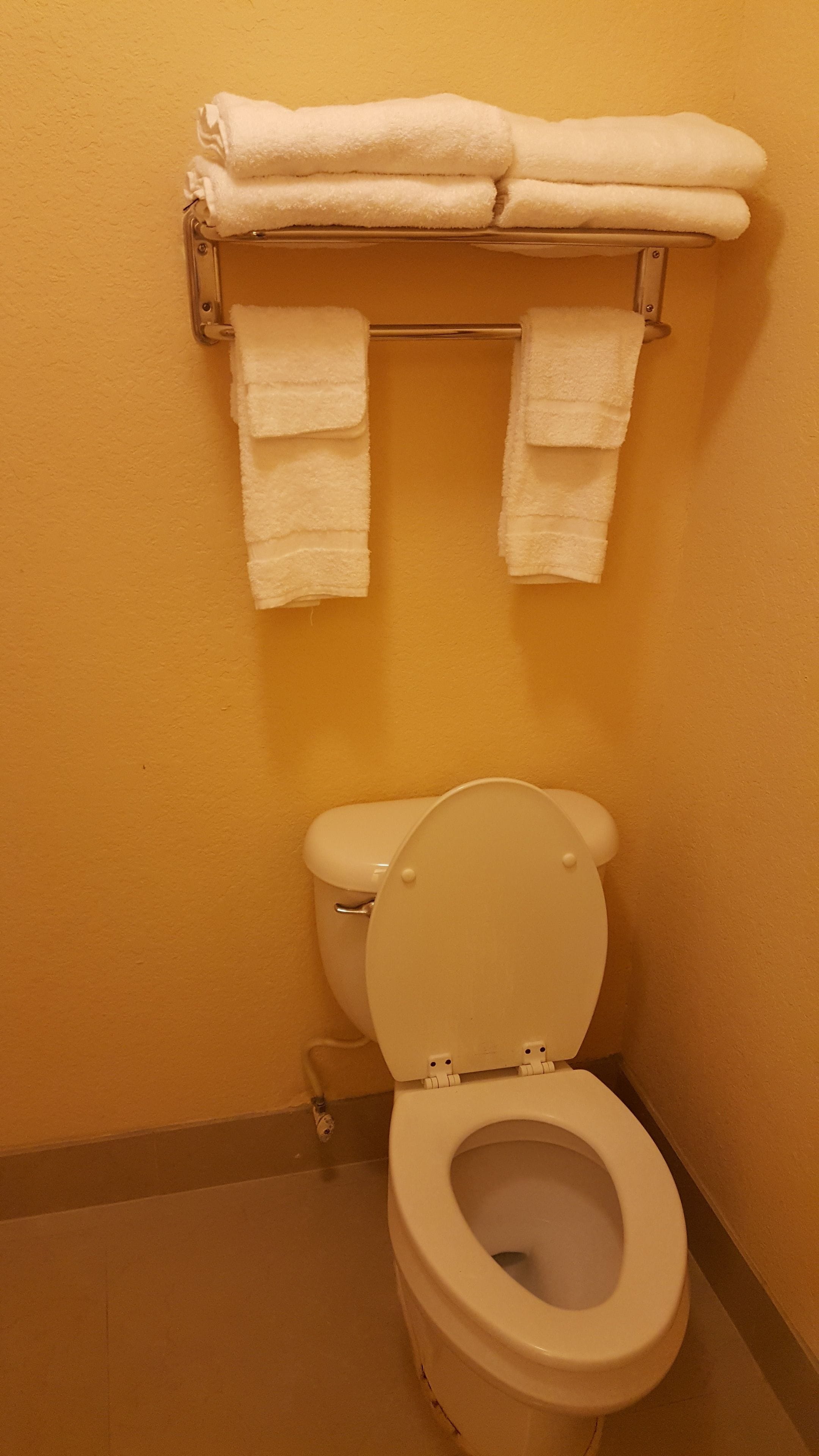 A bathroom with a toilet, a towel rack with folded towels, and a plain yellow wall.