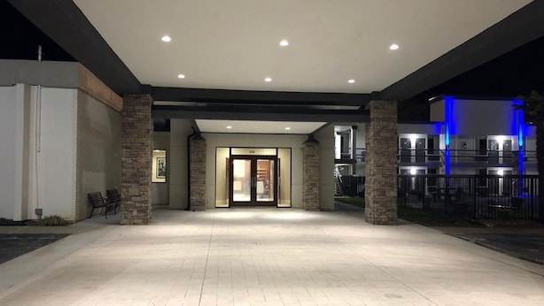 L’entrée d’un hôtel, avec des piliers en pierre, une allée couverte et un bâtiment illuminé de lumière bleue en arrière-plan.