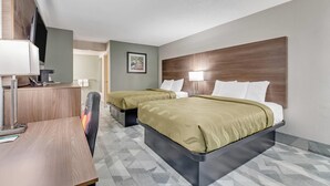 Une chambre d’hôtel avec deux lits, un bureau avec un ordinateur, une télévision et un tableau encadré au mur.