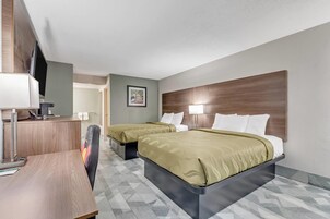 A hotel room with two beds, a desk with a computer, a TV, and a framed picture on the wall.