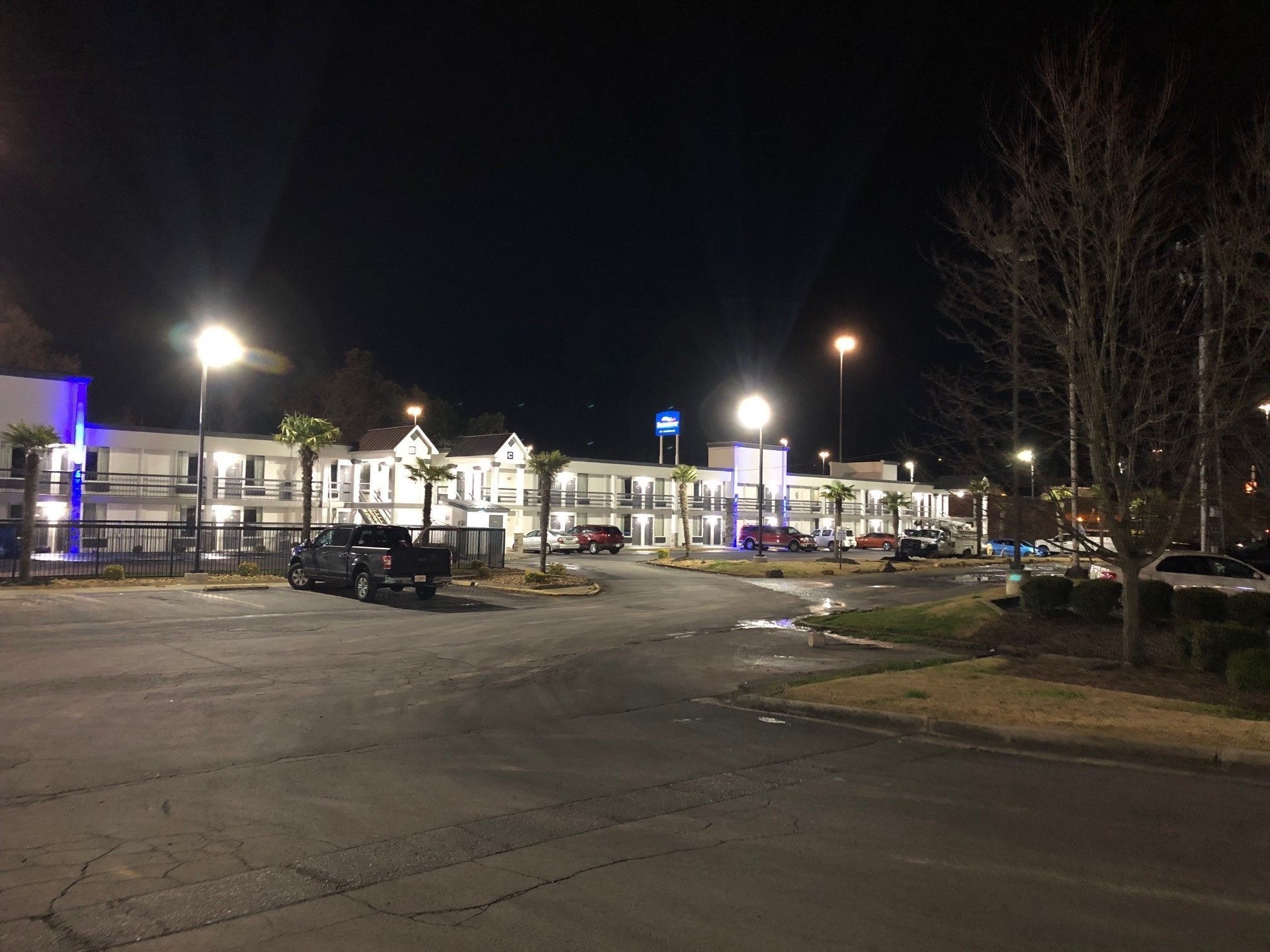 A multi-story hotel with a parking lot, illuminated by street lamps.