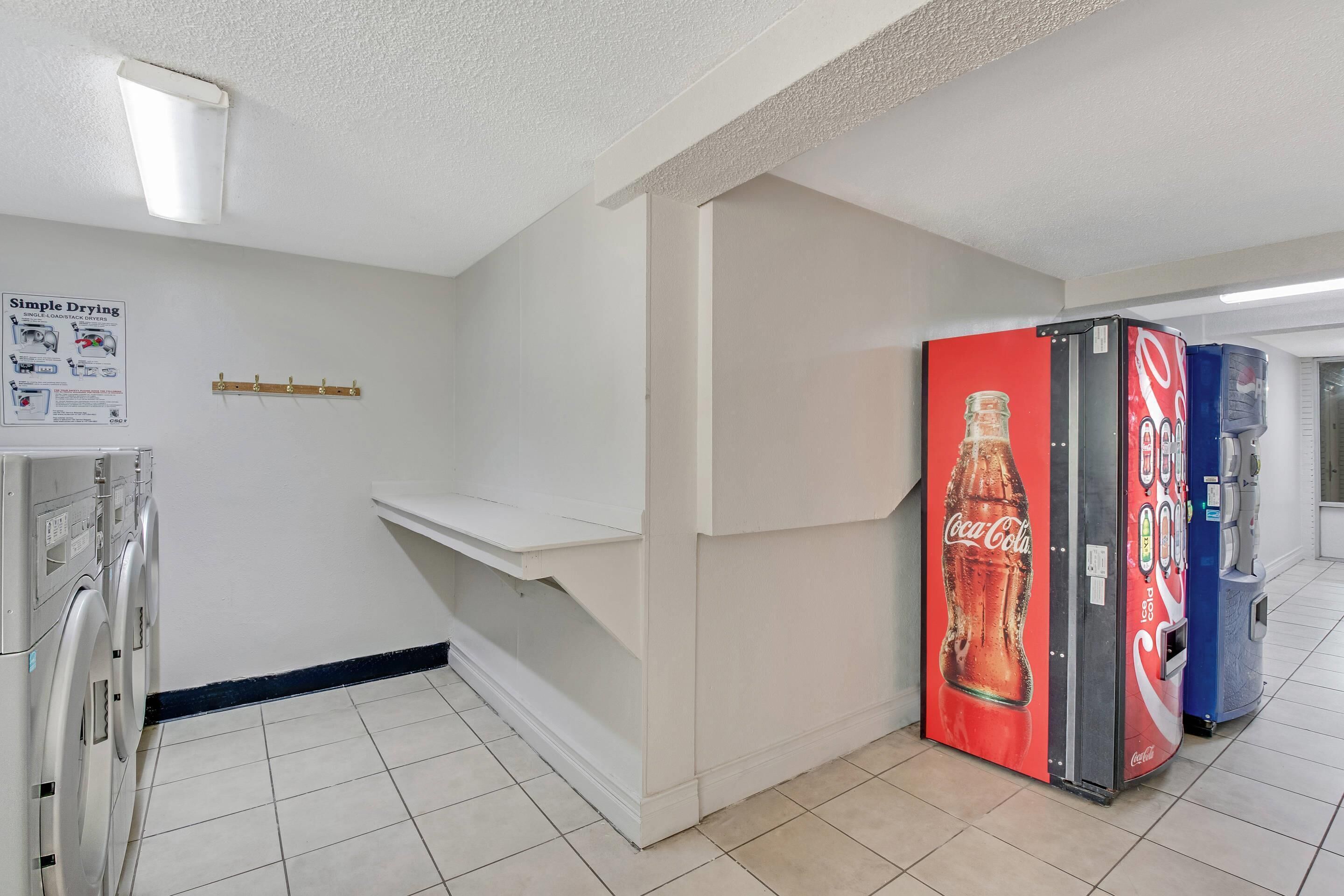 A hallway with a vending machine, a single-load stack dryer, and a wall-mounted shelf.