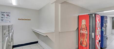 A hallway with a vending machine, a single-load stack dryer, and a wall-mounted shelf.