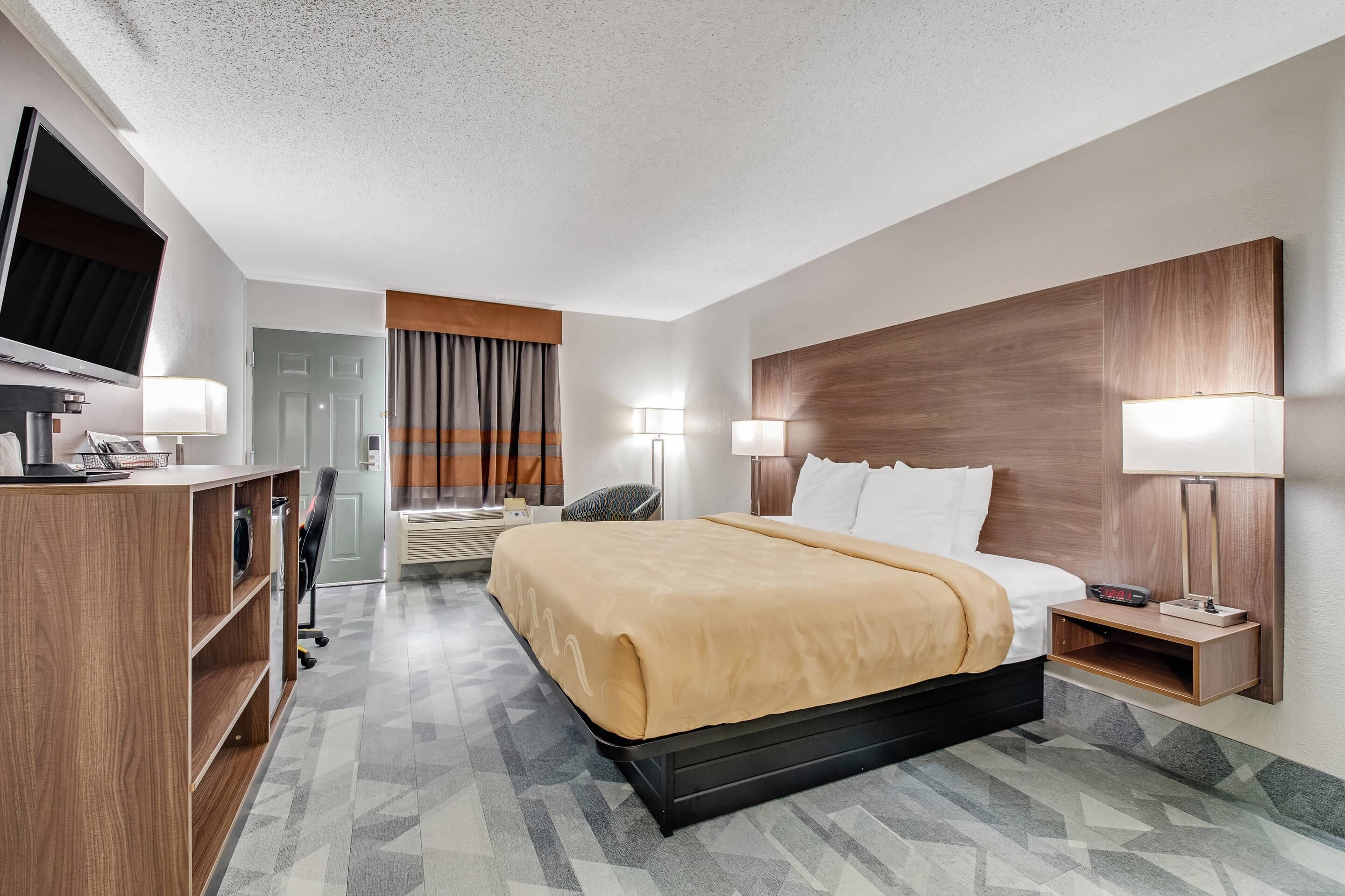 Ein Hotelzimmer mit einem Bett, Nachttischlampen, einem Fernseher, einem Schreibtisch mit Stuhl und einem Kleiderschrank.