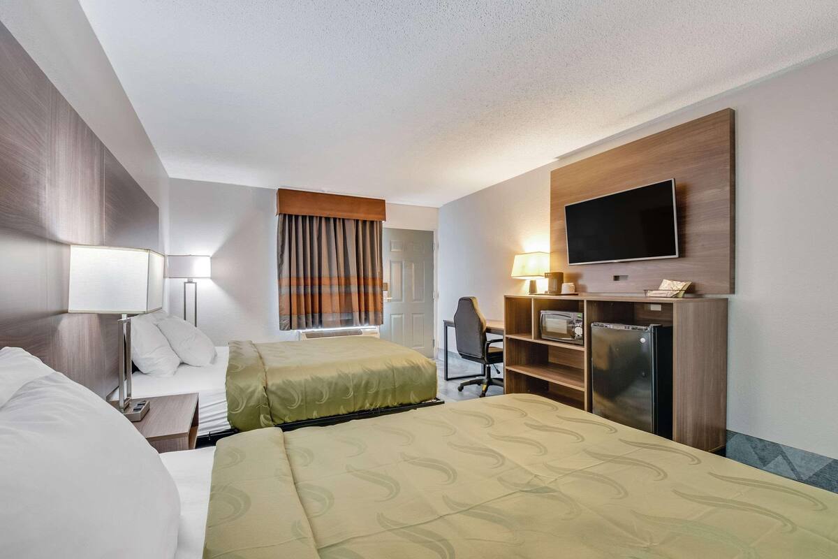 Une chambre d’hôtel avec deux lits, un bureau, une chaise, une télévision et un mini-bar.