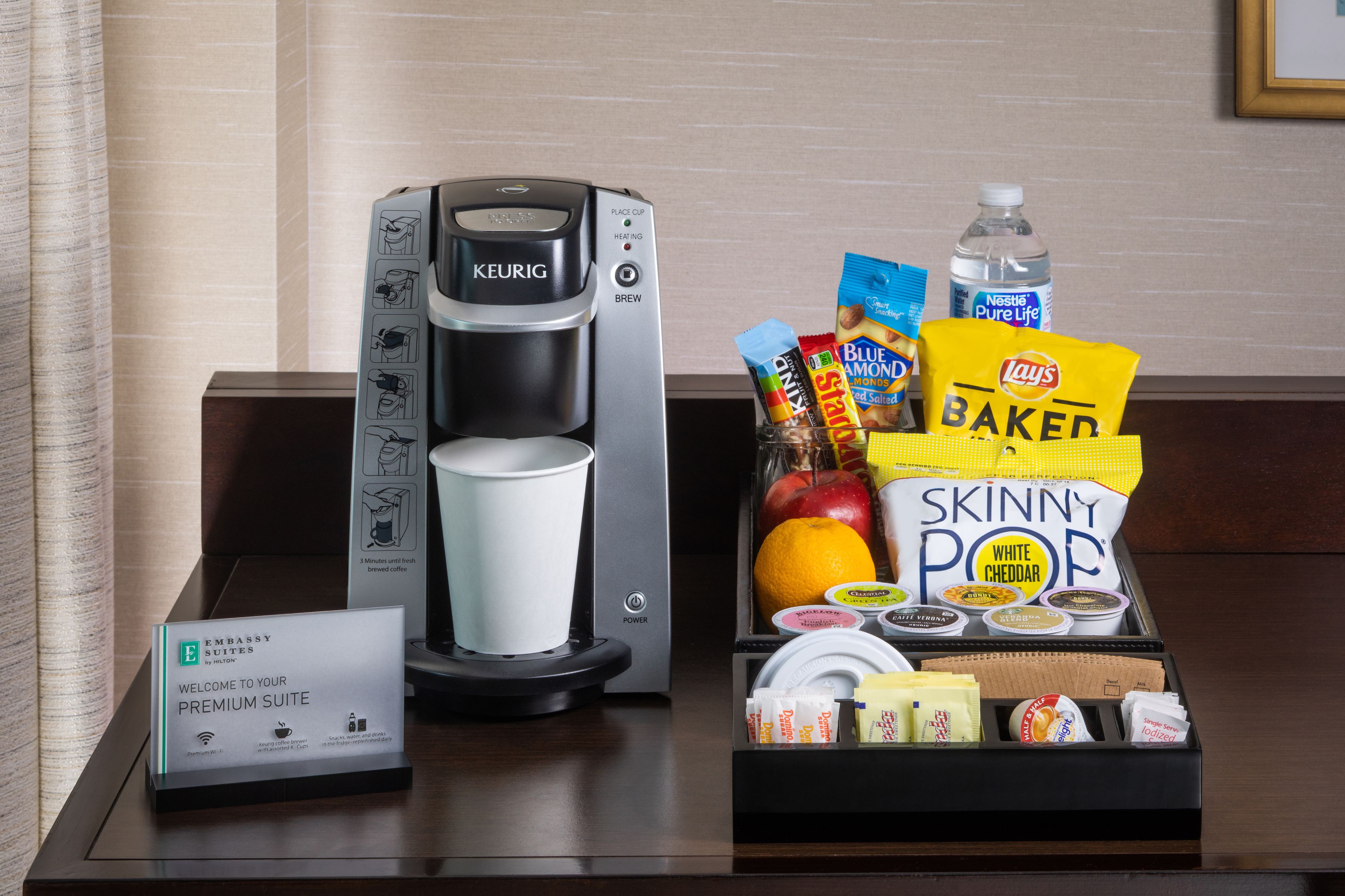 A coffee maker, a tray with snacks, and a welcome sign in a hotel room.
