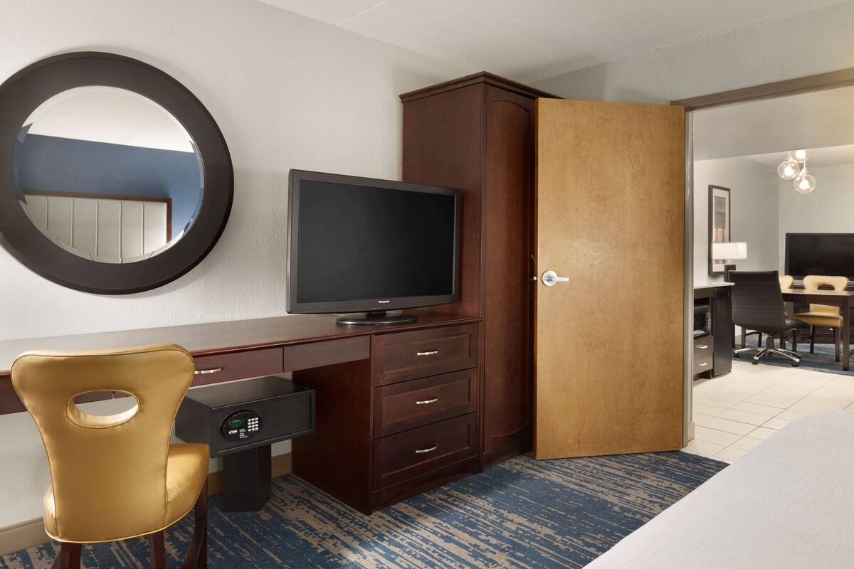 A hotel room with a television, a desk with a computer, a chair, a wardrobe, and a bed.