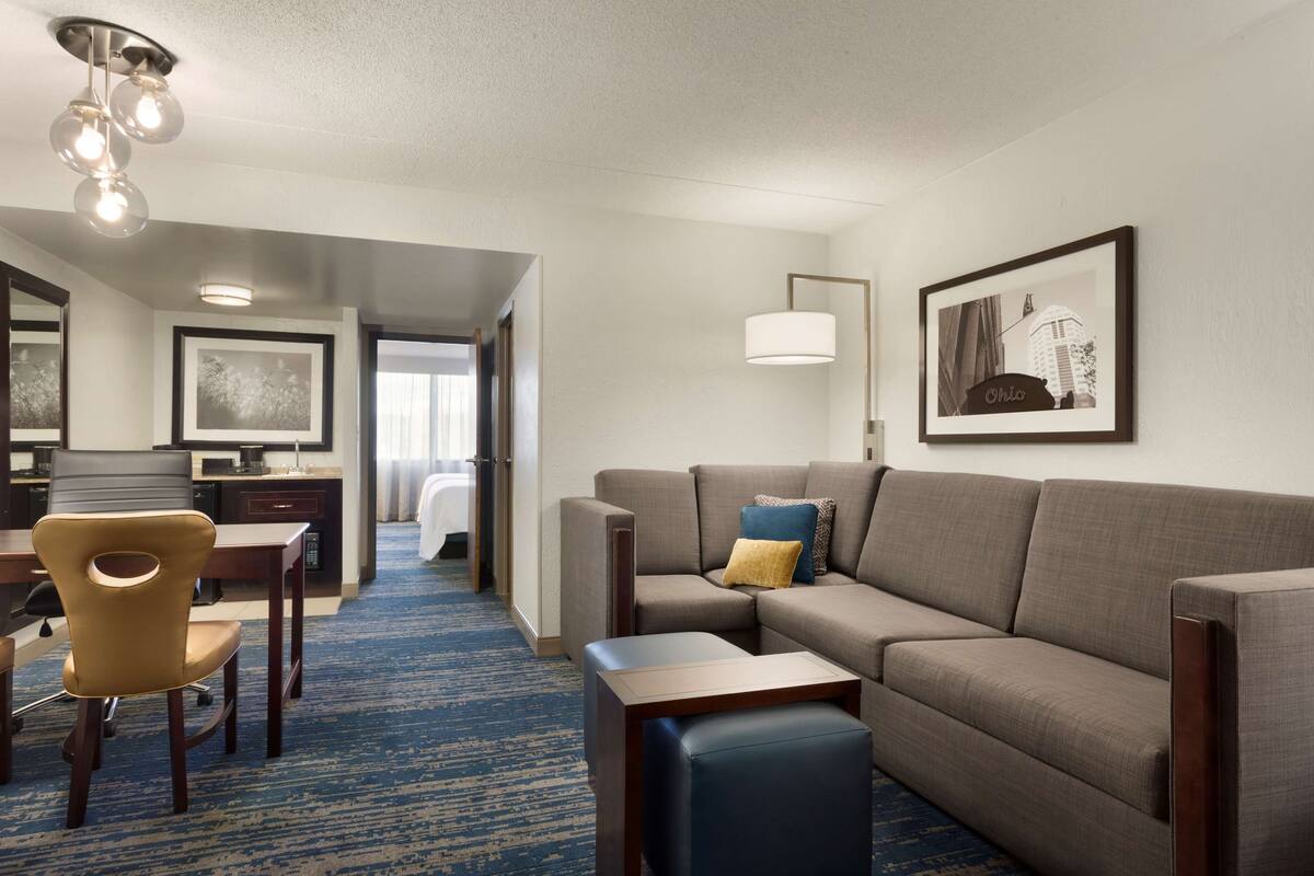 A hotel room with a sofa, a chair, a small table, a lamp, and a framed picture on the wall.