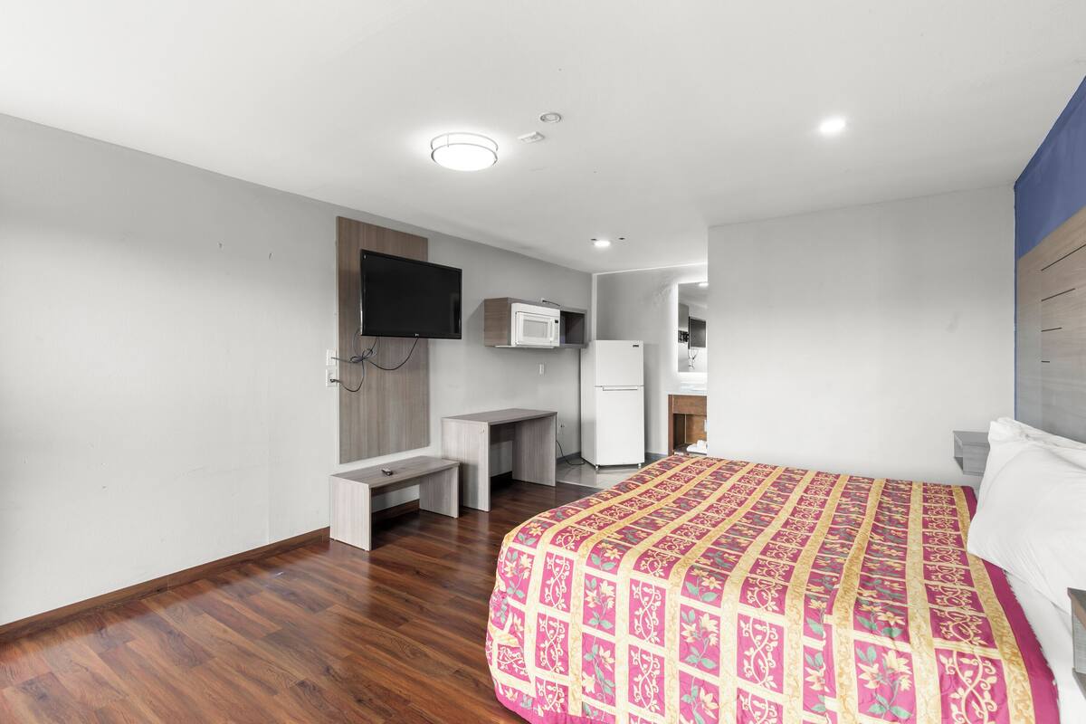 A hotel room with a bed, a desk, a television, and a microwave.