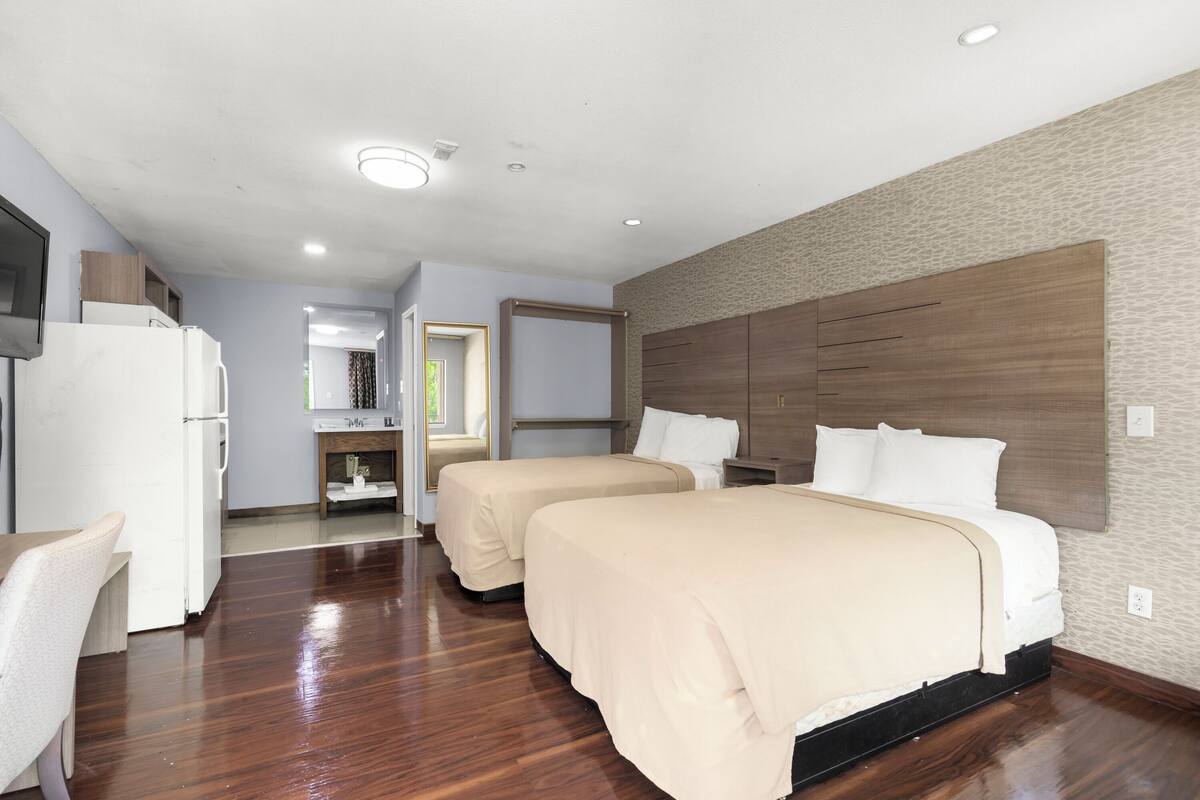A hotel room with two beds, a kitchenette, a bathroom, and a dining area.